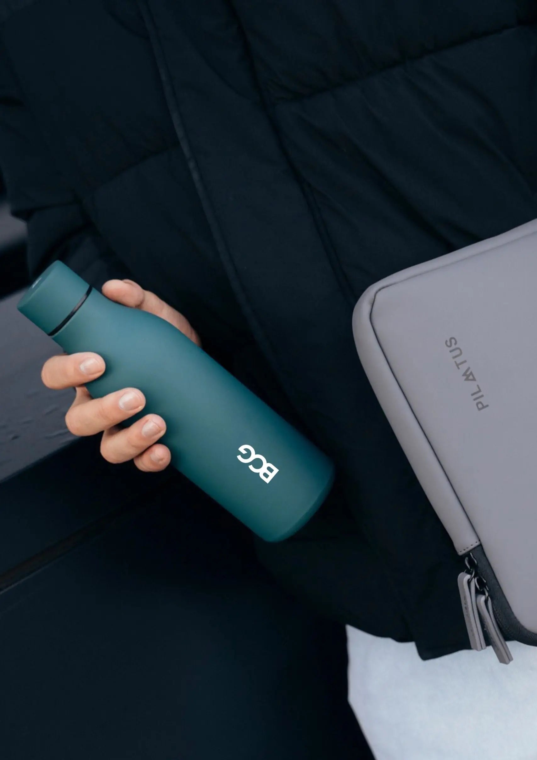 Botella térmica dark green Pilatus Brand con logotipo de BCG sostenida por una persona con chaqueta de invierno negra.