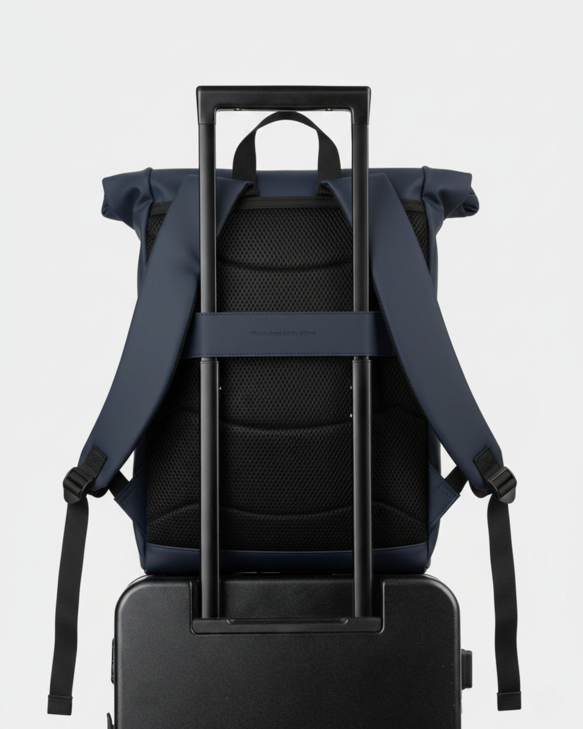Mochila azul marino sujeta al tirador telescópico de una maleta negra; respaldo acolchado de malla y correas colgando
