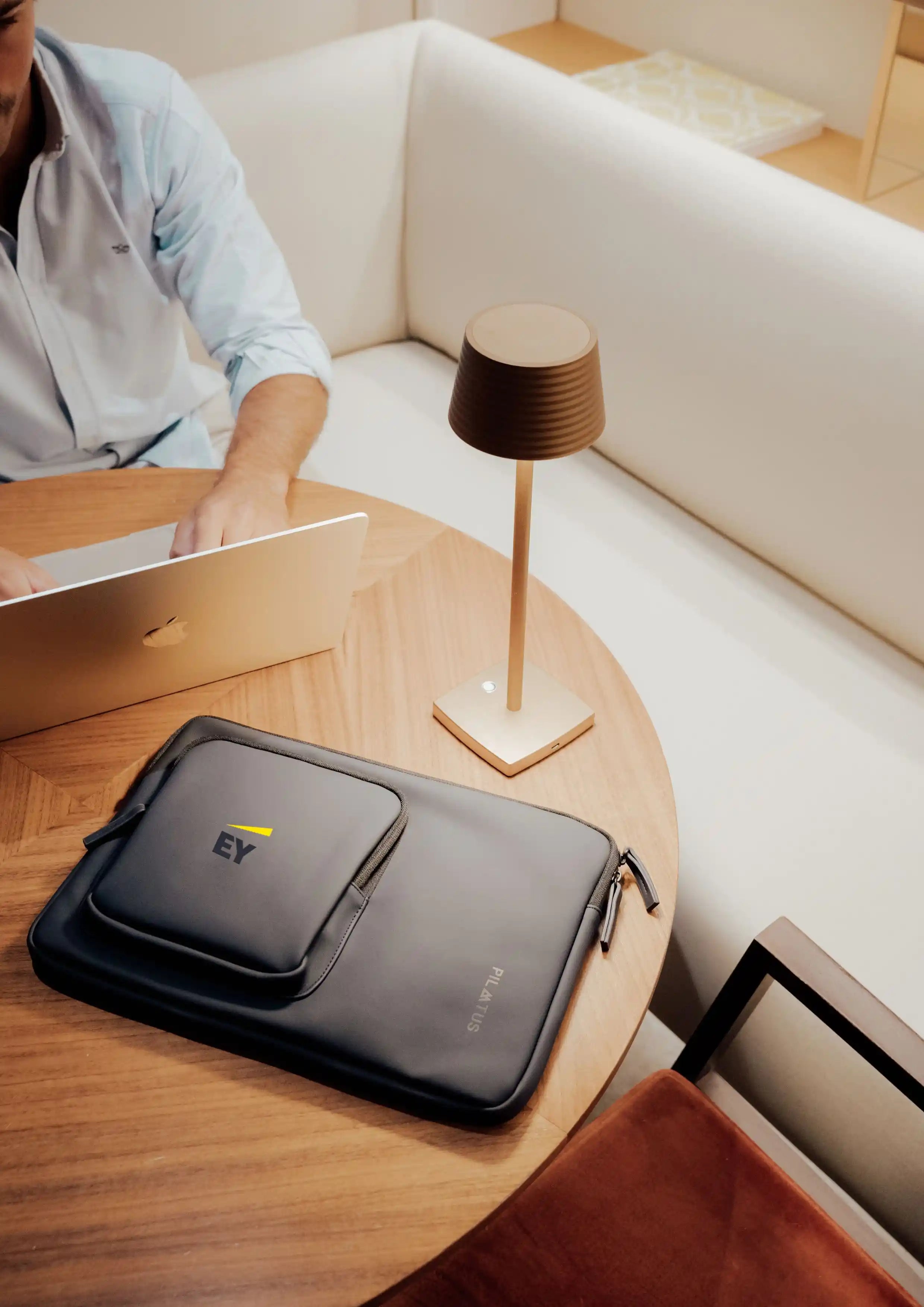 Hombre tecleando en su portátil y con funda personalizada Urban Sleeve en color Blue Navy con el logotipo de EY sobre la mesa.