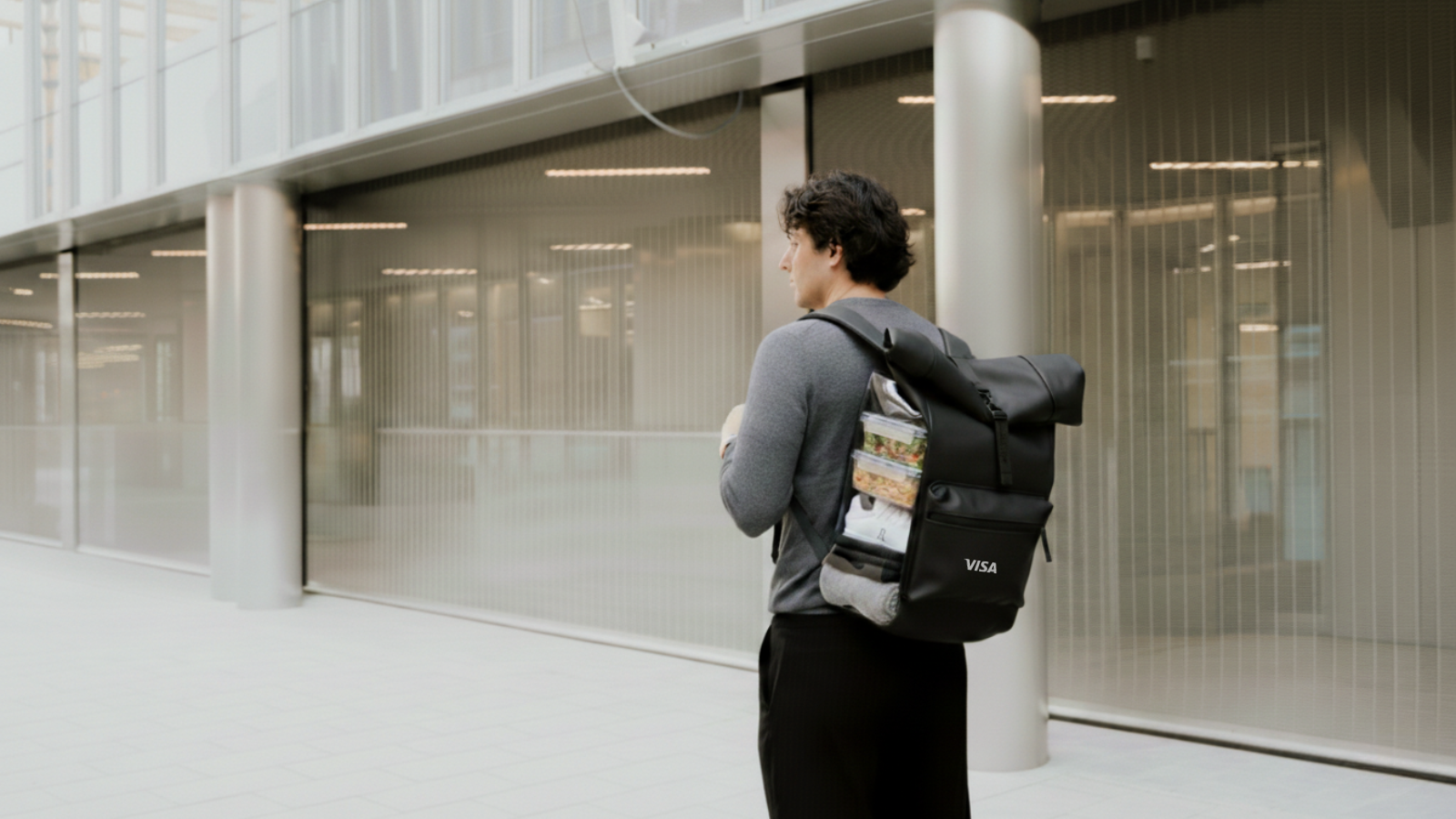 Hombre moreno con mochila urban negra y con el logo de la empresa Visa.