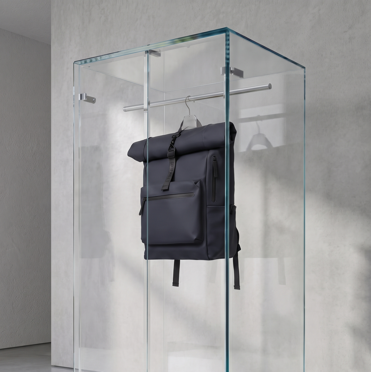 Mochila roll-top azul oscuro con bolsillo frontal y cremallera, colgada de un gancho metálico dentro de una vitrina
