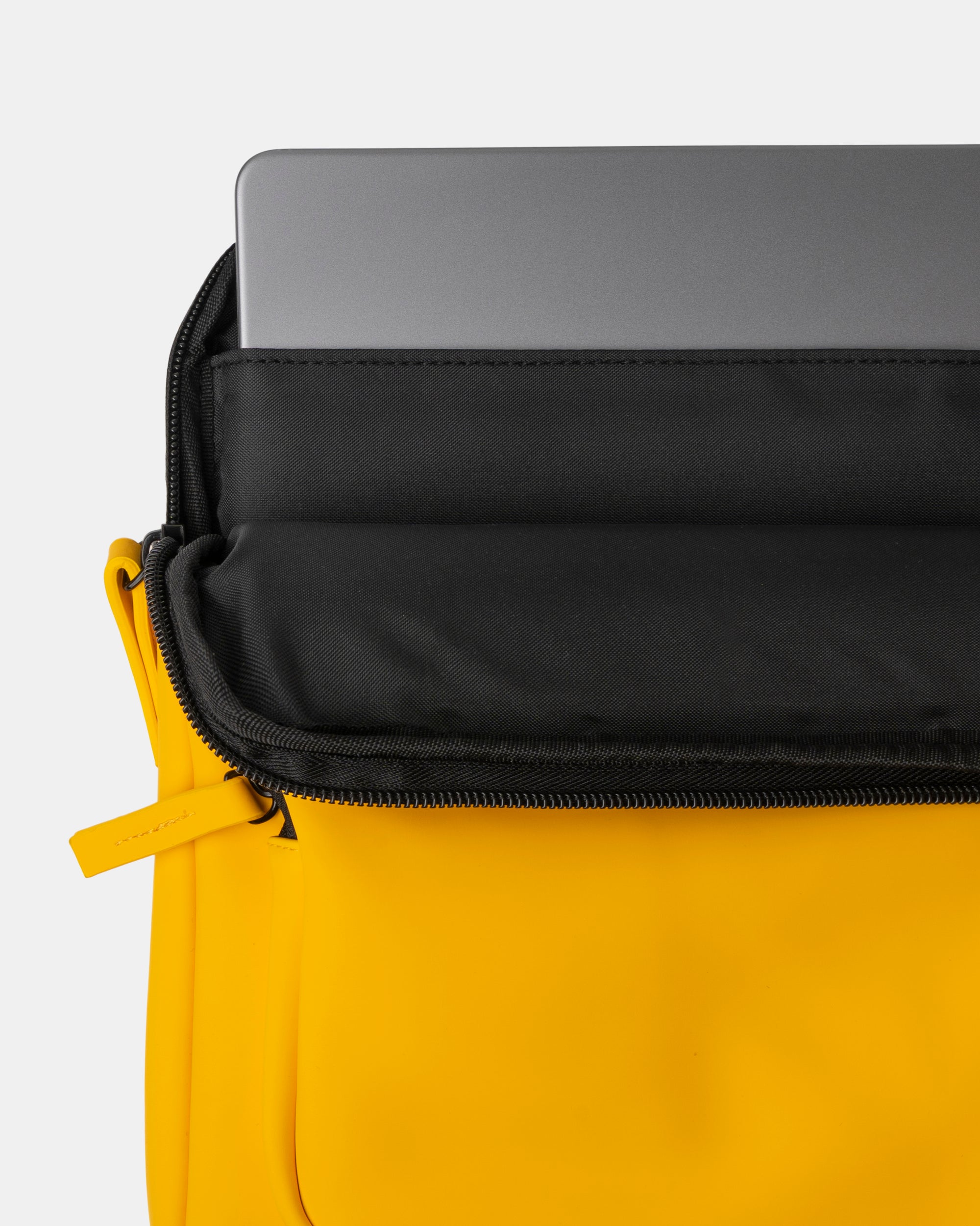 Mochila amarilla con cremallera abierta, bolsillo interior negro para portátil con un portátil gris parcialmente insertado