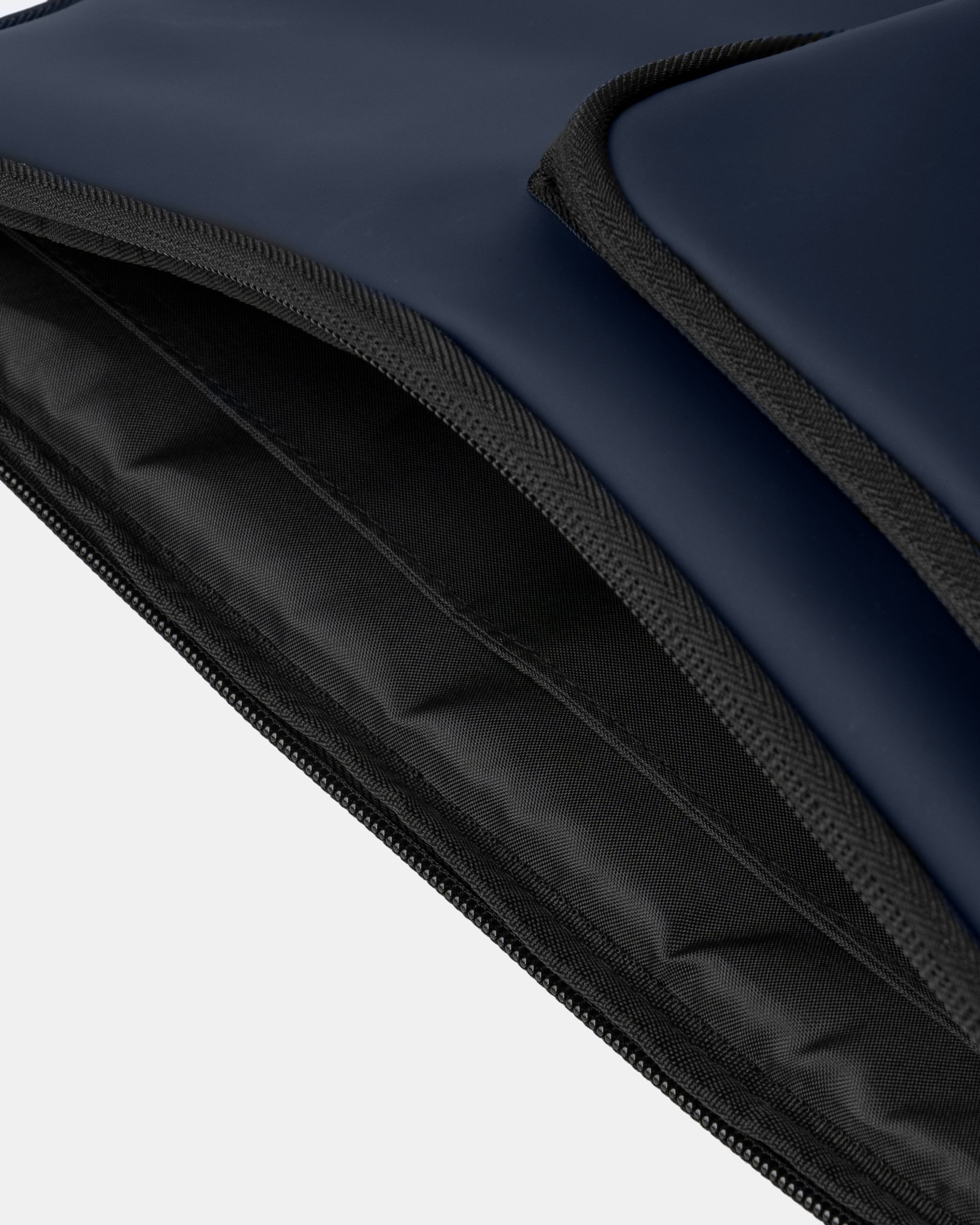 Bolsillo acolchado de mochila azul marino con ribetes negros; interior forrado de nylon negro y cierre de cremallera visible