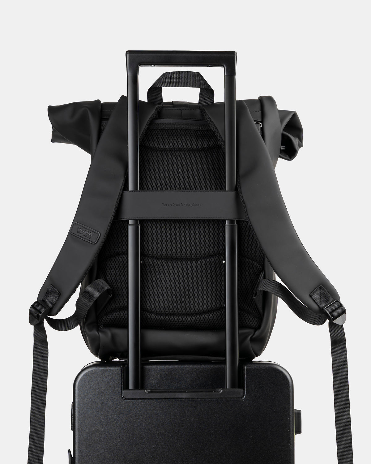 Mochila negra con respaldo acolchado y correas, montada sobre el tirador telescópico de una maleta. Texto: PILATUS (etiqueta)