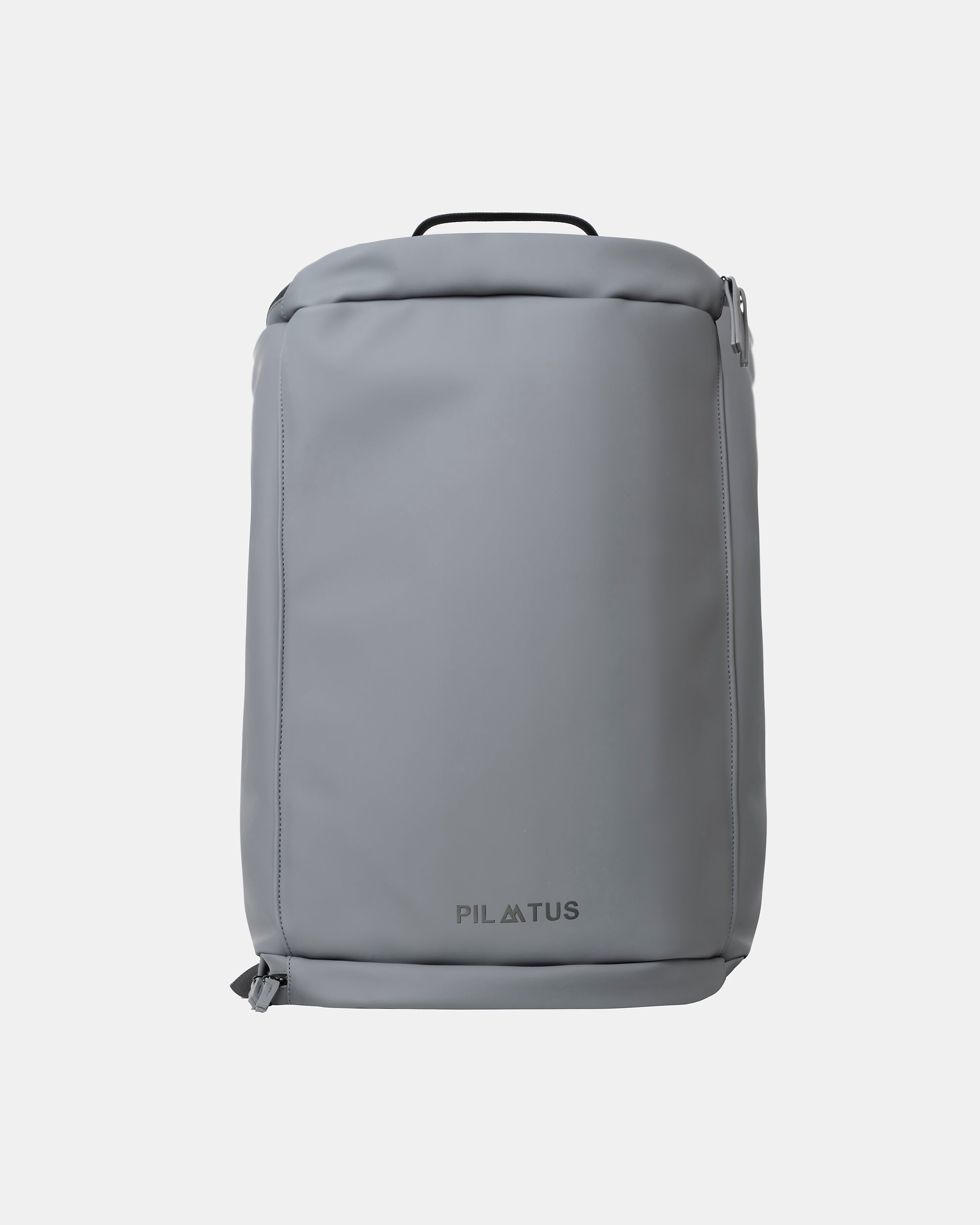 Mochila gris rectangular de exterior liso; asa superior y cremalleras visibles sobre fondo blanco minimalista. Texto: PILATUS
