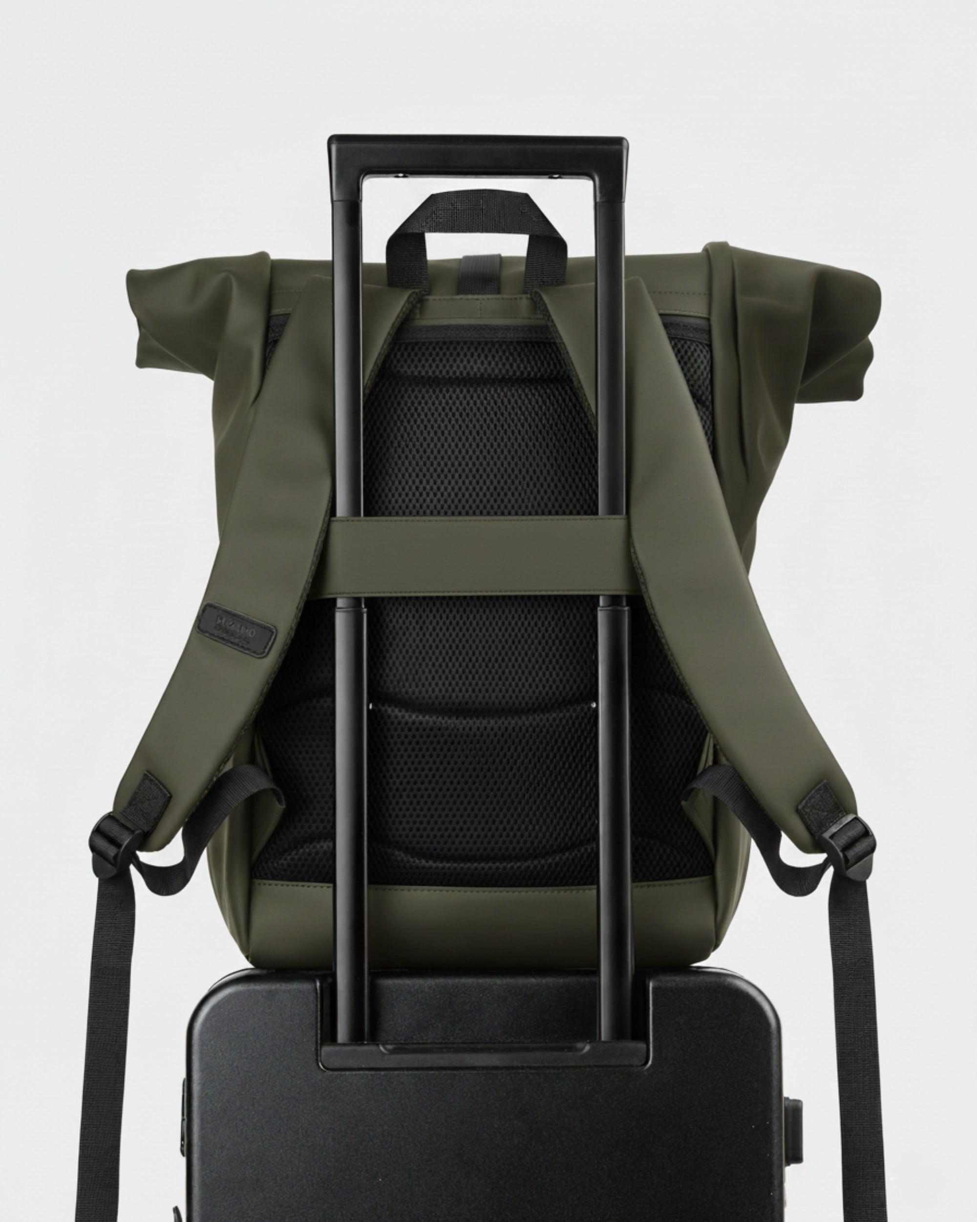 Mochila roll-top verde oliva enganchada al tirador telescópico de una maleta; respaldo acolchado negro y correas ajustables