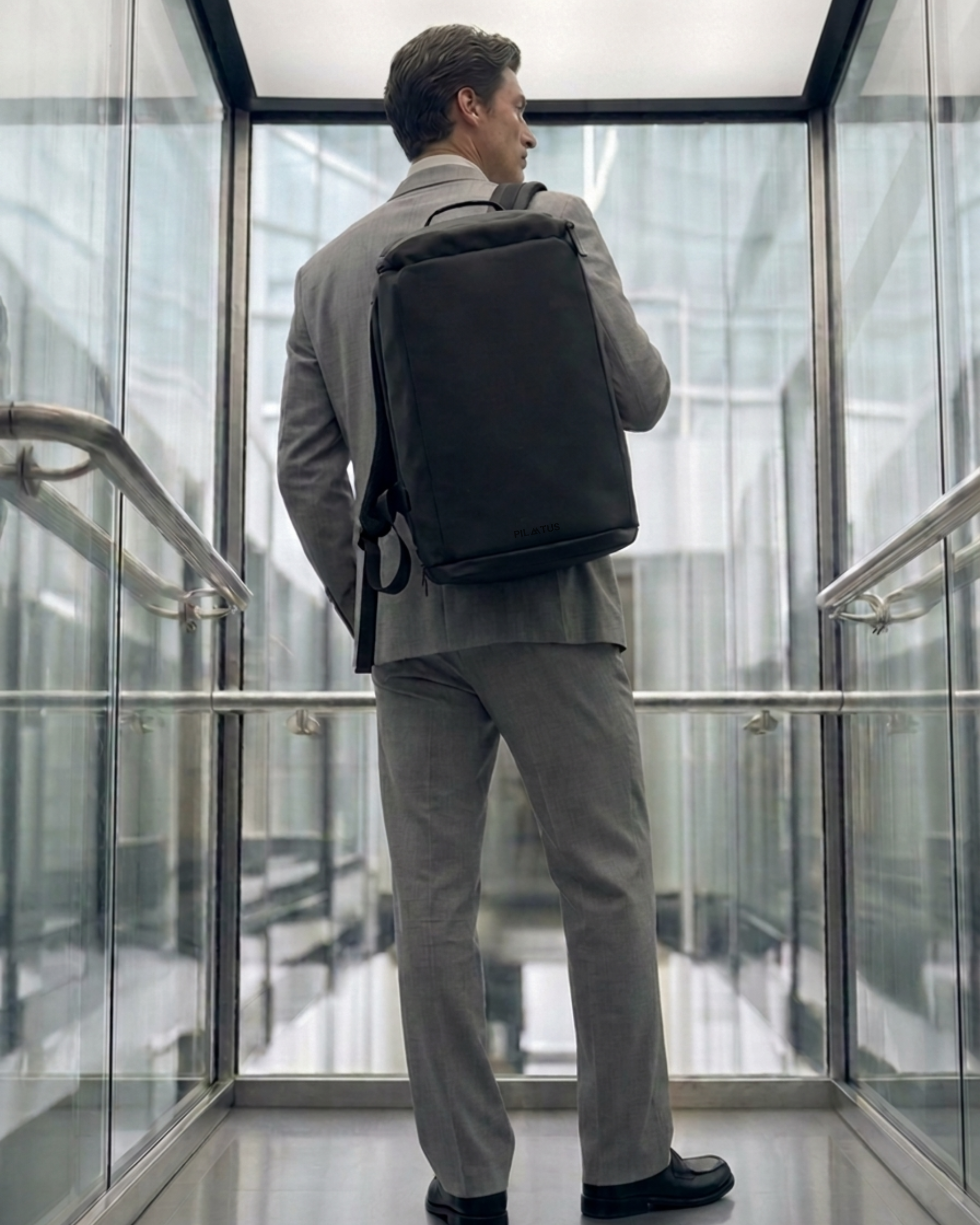 Mochila negra rectangular con logo PILATUS en la base; hombre con traje gris la lleva a la espalda
