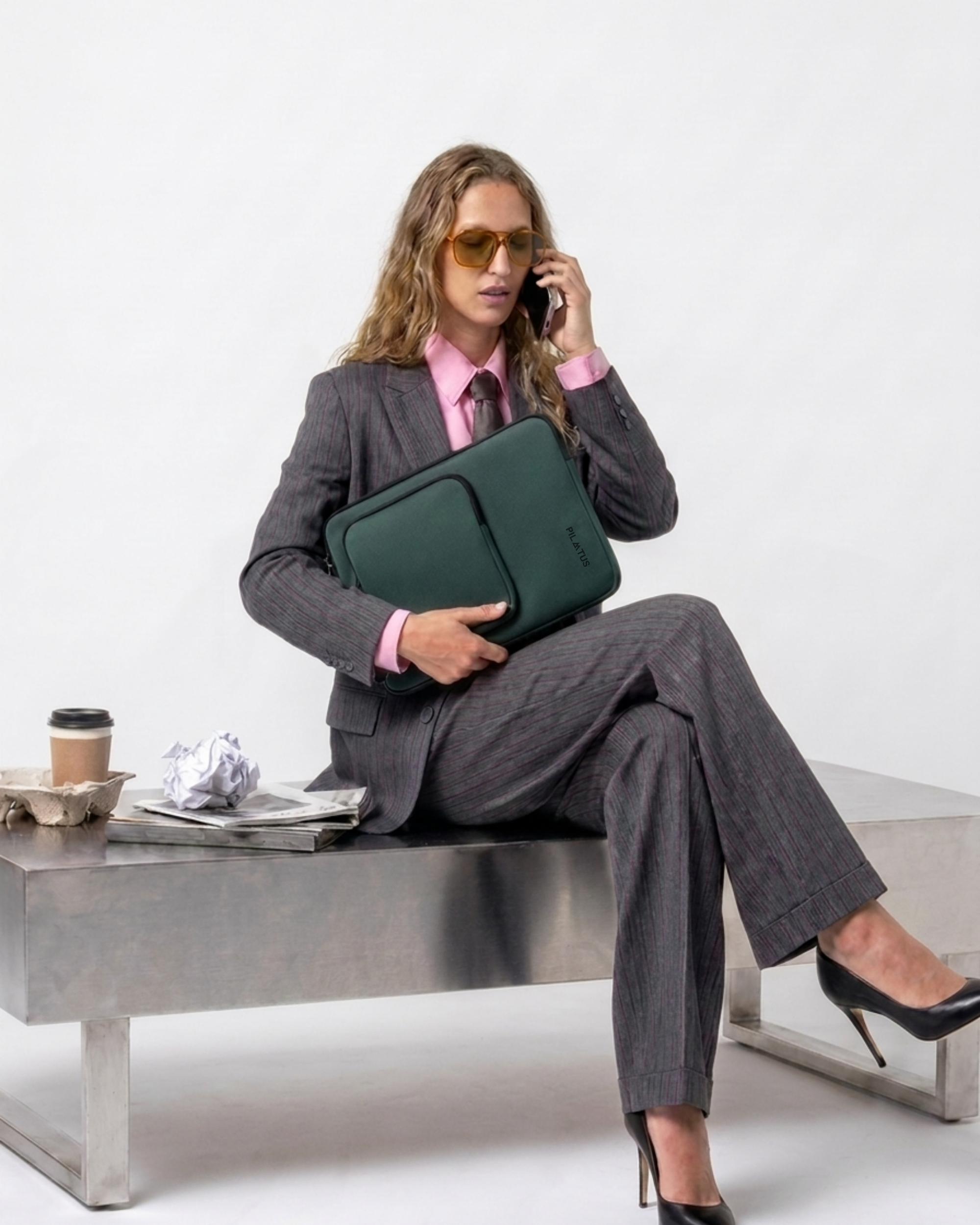 Bolsa para portátil verde con logo PILATUS, sostenida por mujer con traje gris y camisa rosa; gafas amarillas