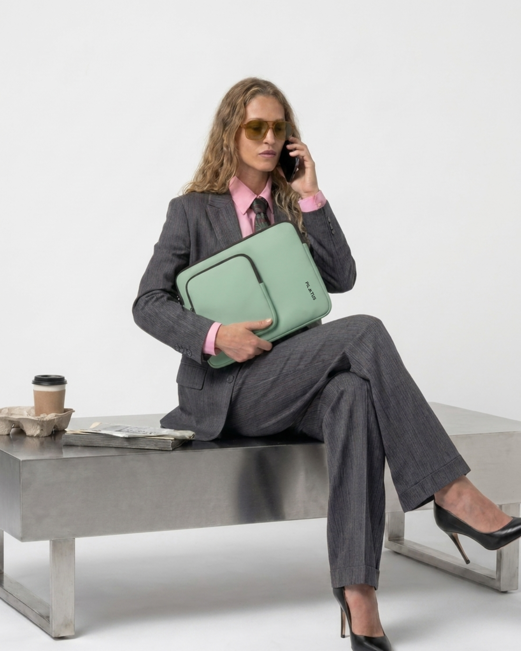 Funda portátil verde menta con logo PILATUS, sostenida por mujer vestida con traje gris y camisa rosa; está sentada