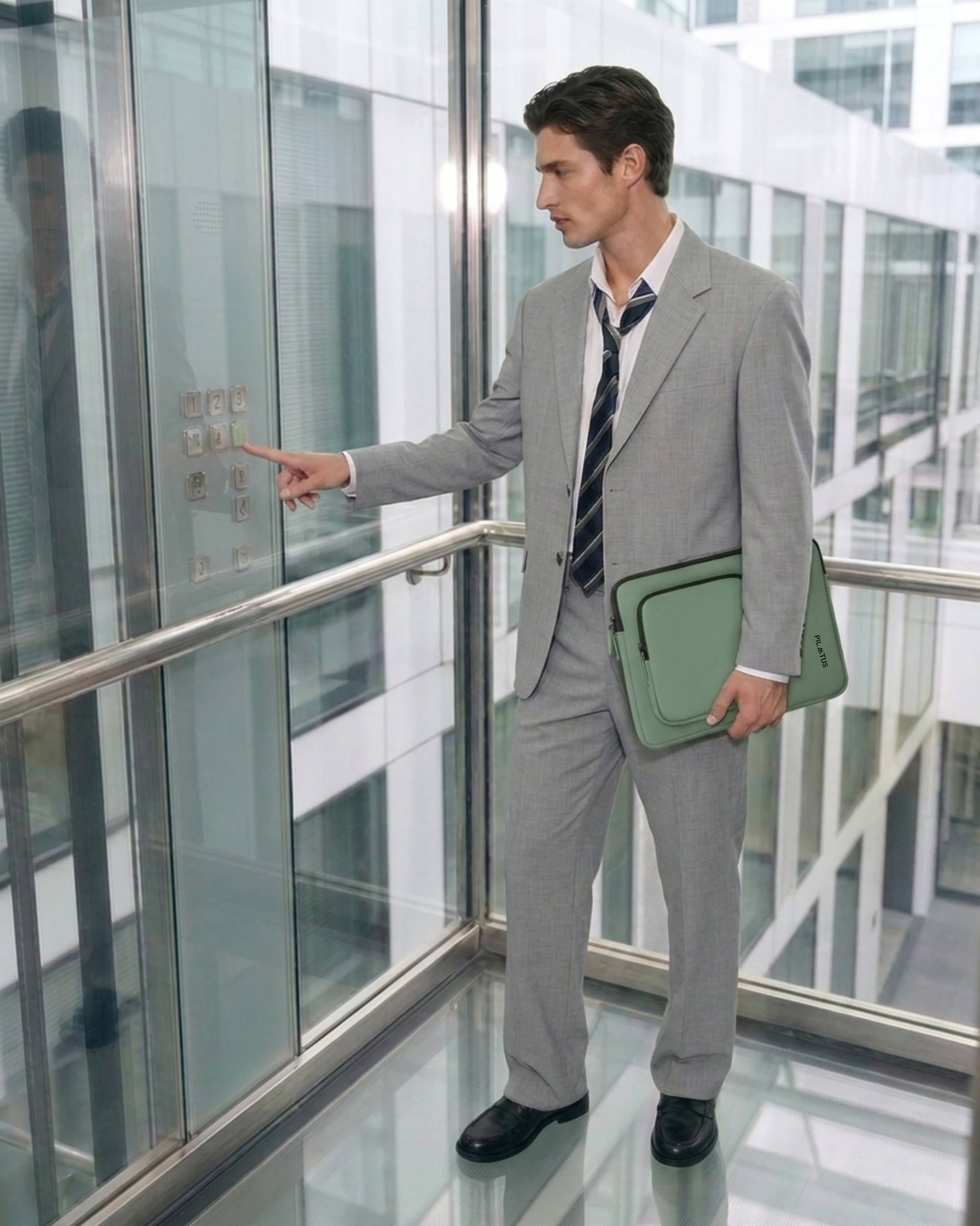 Funda para portátil verde sujeta por un hombre de traje en ascensor de cristal, pulsando un botón. Texto: PILATUS
