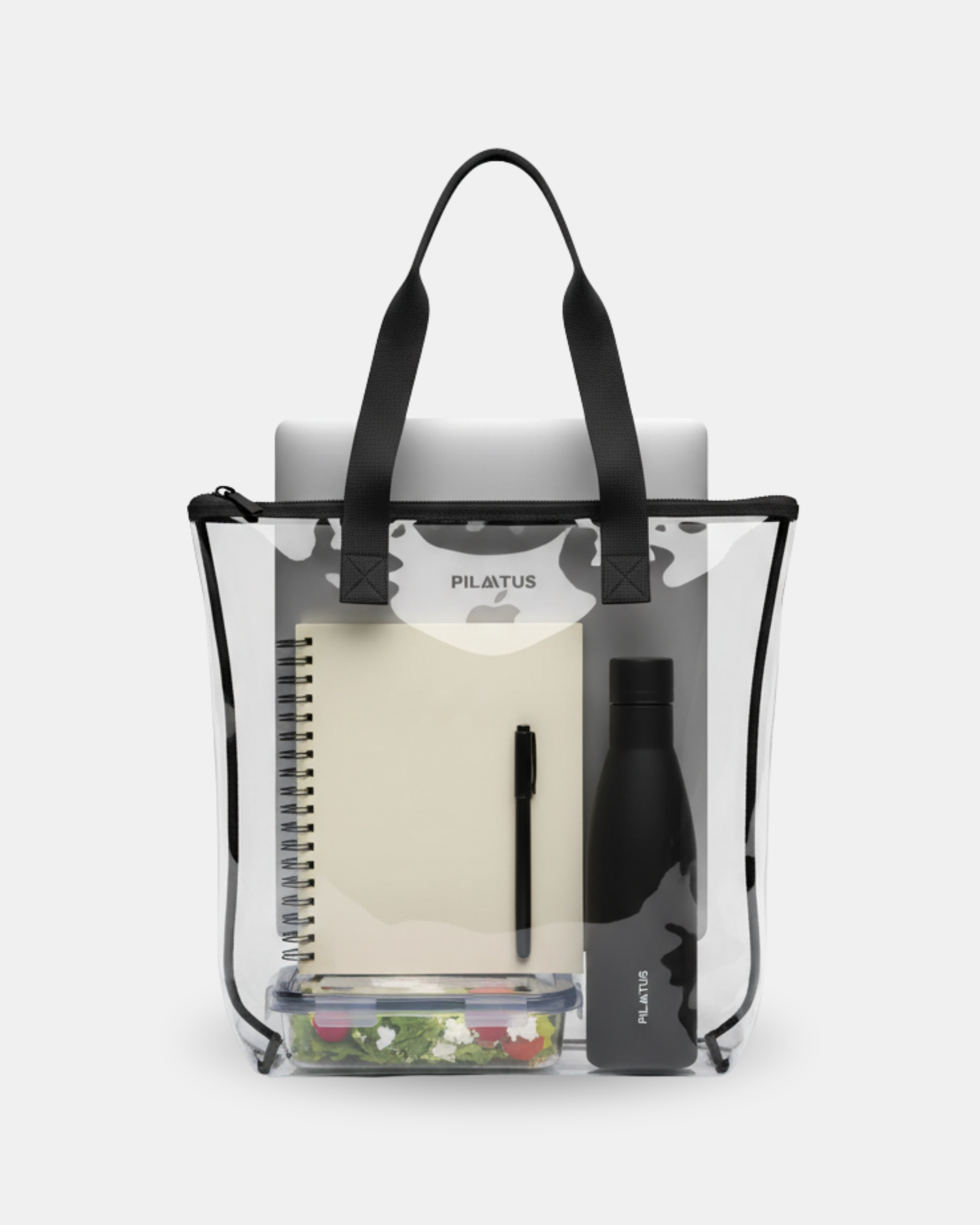 Bolsa transparente con asas negras: contiene libreta espiral, bolígrafo, botella térmica negra y fiambrera; sobre fondo claro