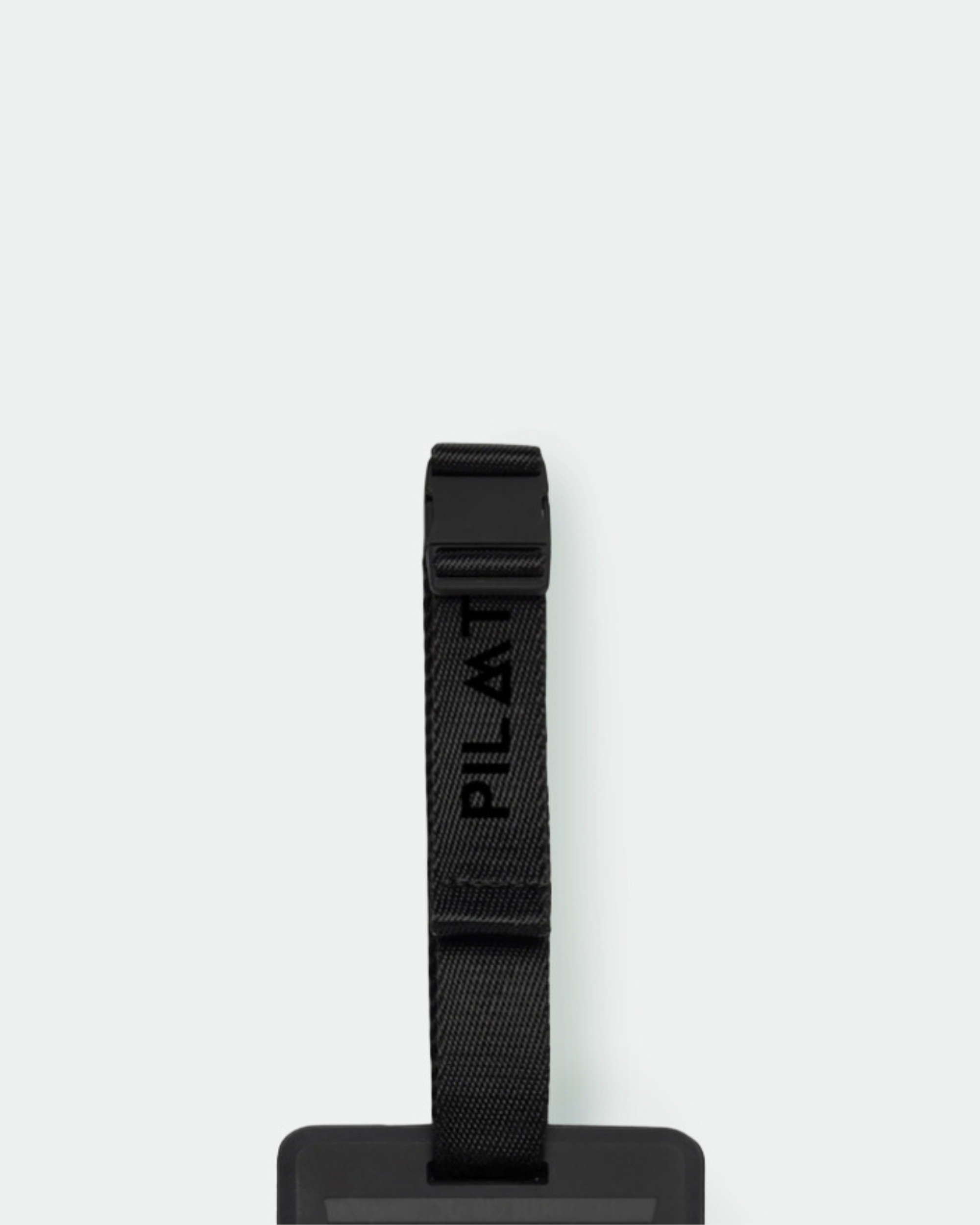 Etiqueta colgante negra con cinta y hebilla ajustable sobre fondo blanco liso. Texto: PILATUS