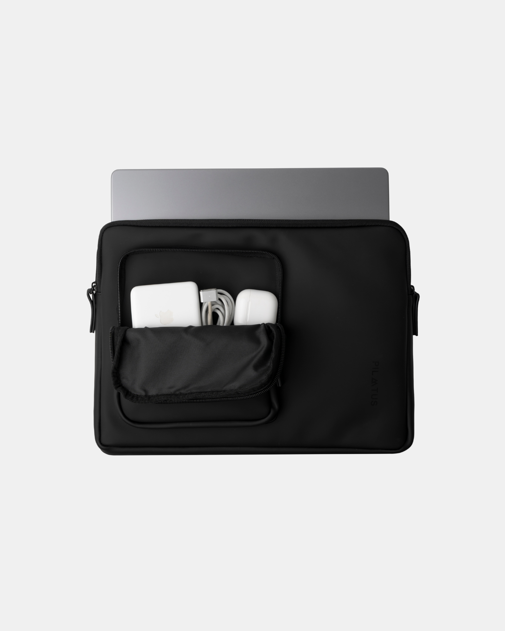 Bolsa portaordenador negra con bolsillo frontal abierto que contiene cargador Apple blanco. Texto: PILATUS