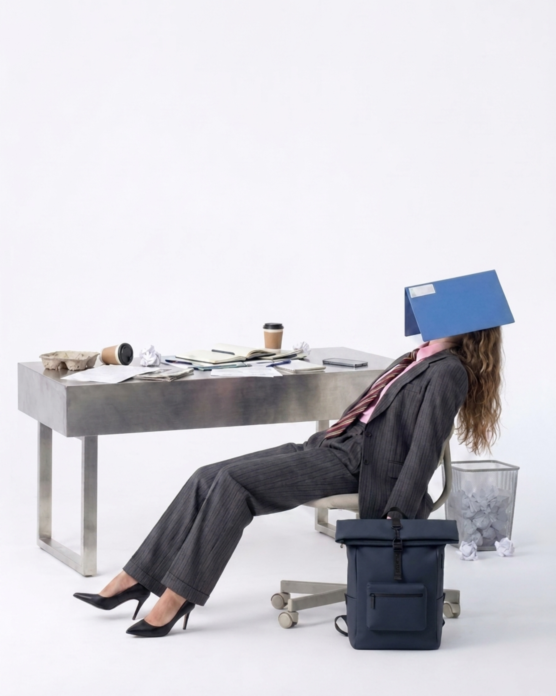 Mochila azul marino en primer plano; mujer con traje recostada y carpeta azul sobre la cabeza. Texto: PILATUS