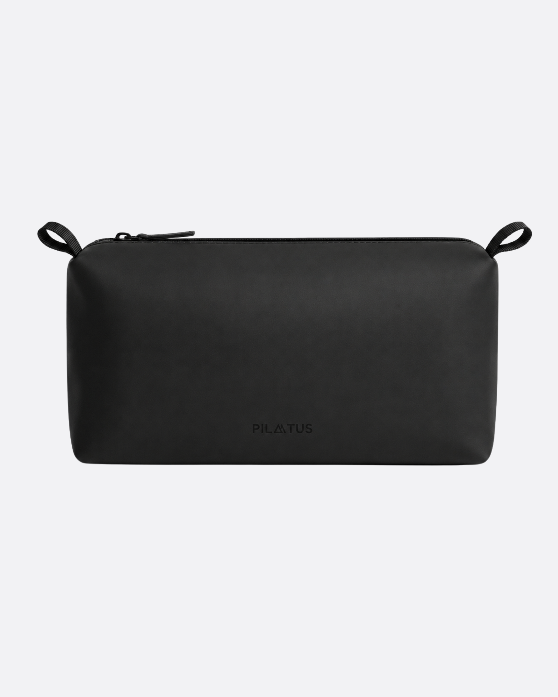 Neceser negro rectangular con cremallera superior y asas de cinta en ambos extremos; sobre fondo gris claro. Texto: PILATUS