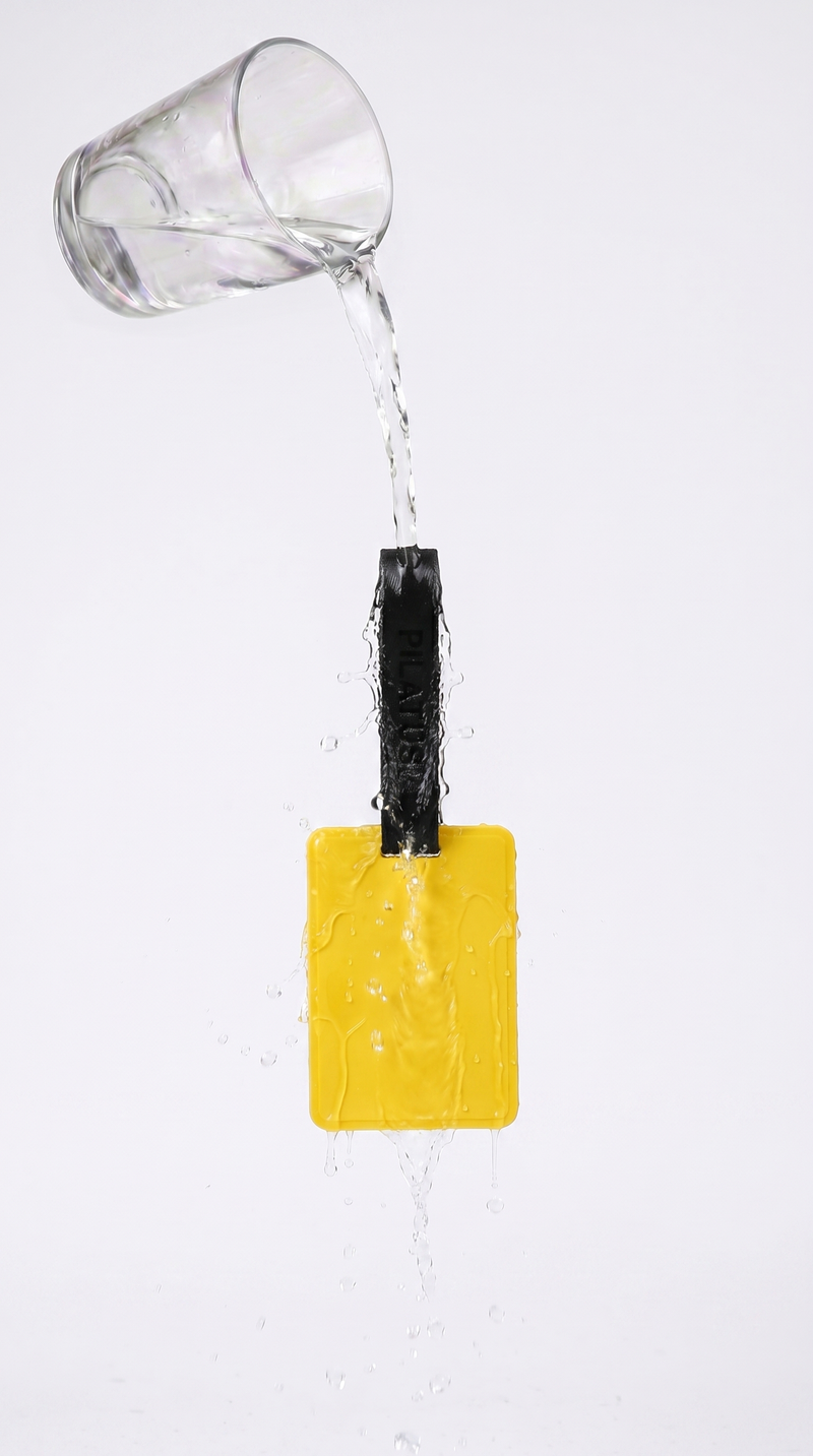 Etiqueta amarilla rectangular con tira negra marcada PILATUS, agua vertida desde un vaso de cristal sobre la tira